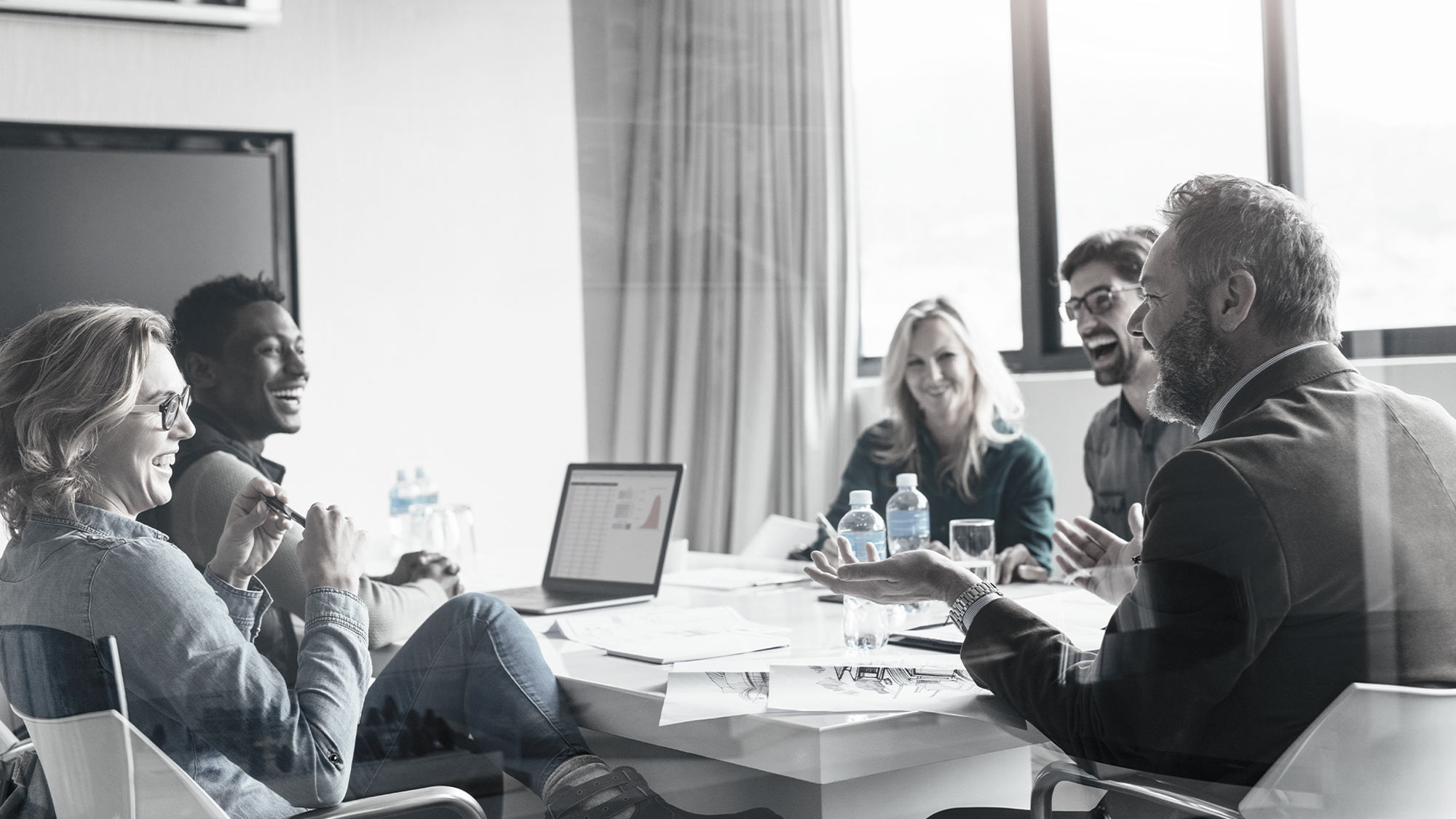 Un homme et deux femmes discutent en souriant devant un ordinateur portable ouvert sur un bureau.