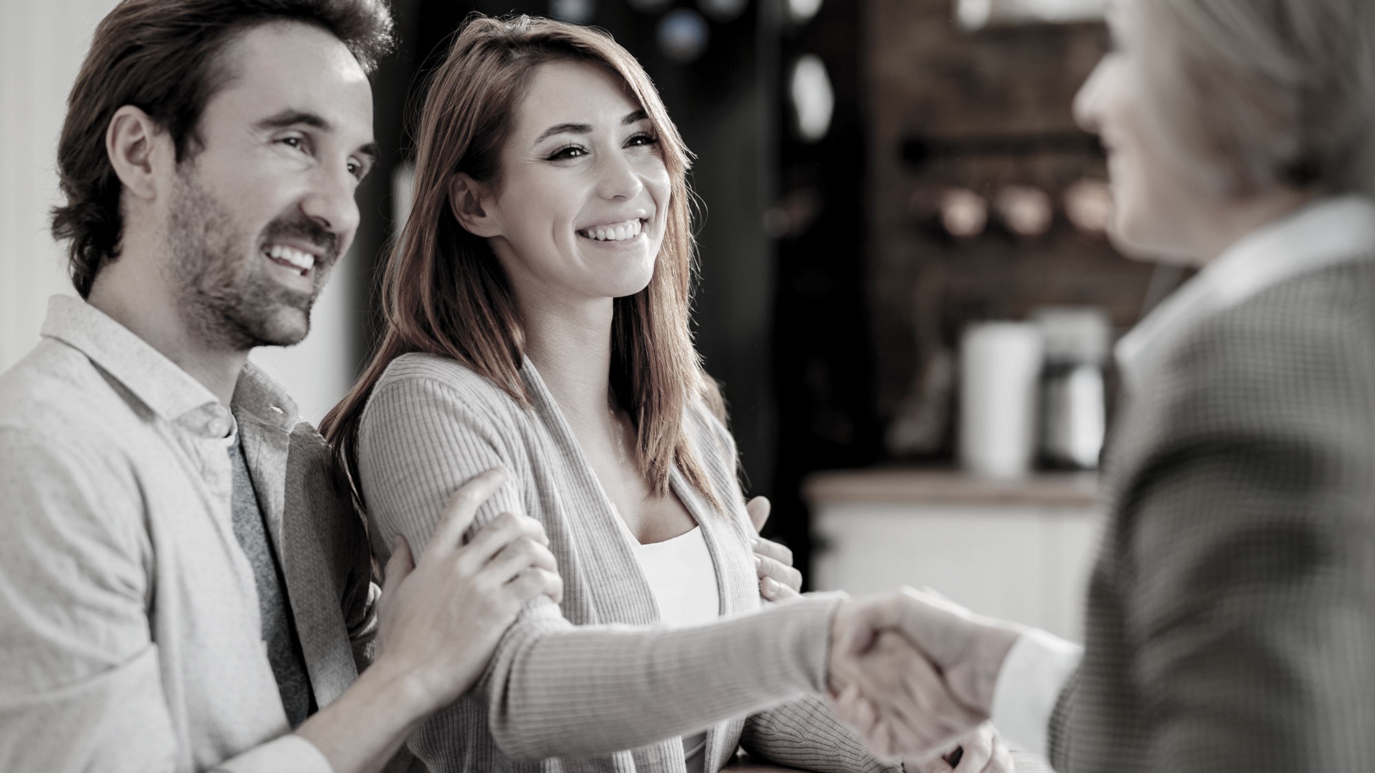 Smiling man and woman talking with another man across a table.